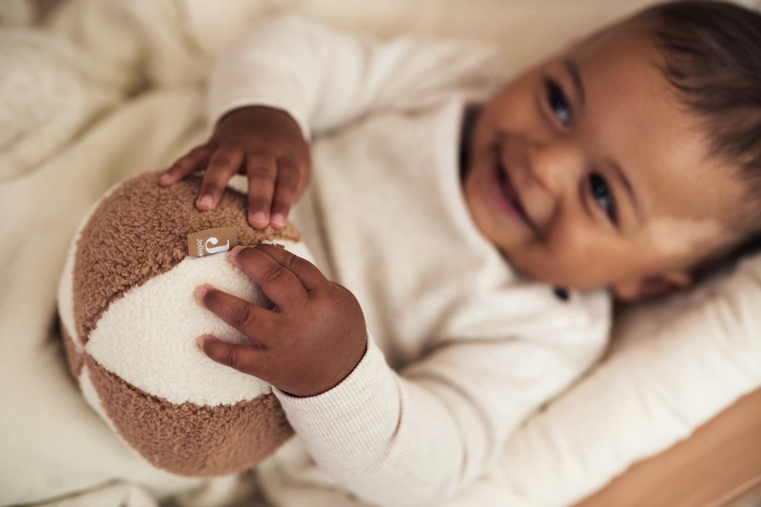 baby holding the Jollein soft play ball in ivory and biscuit