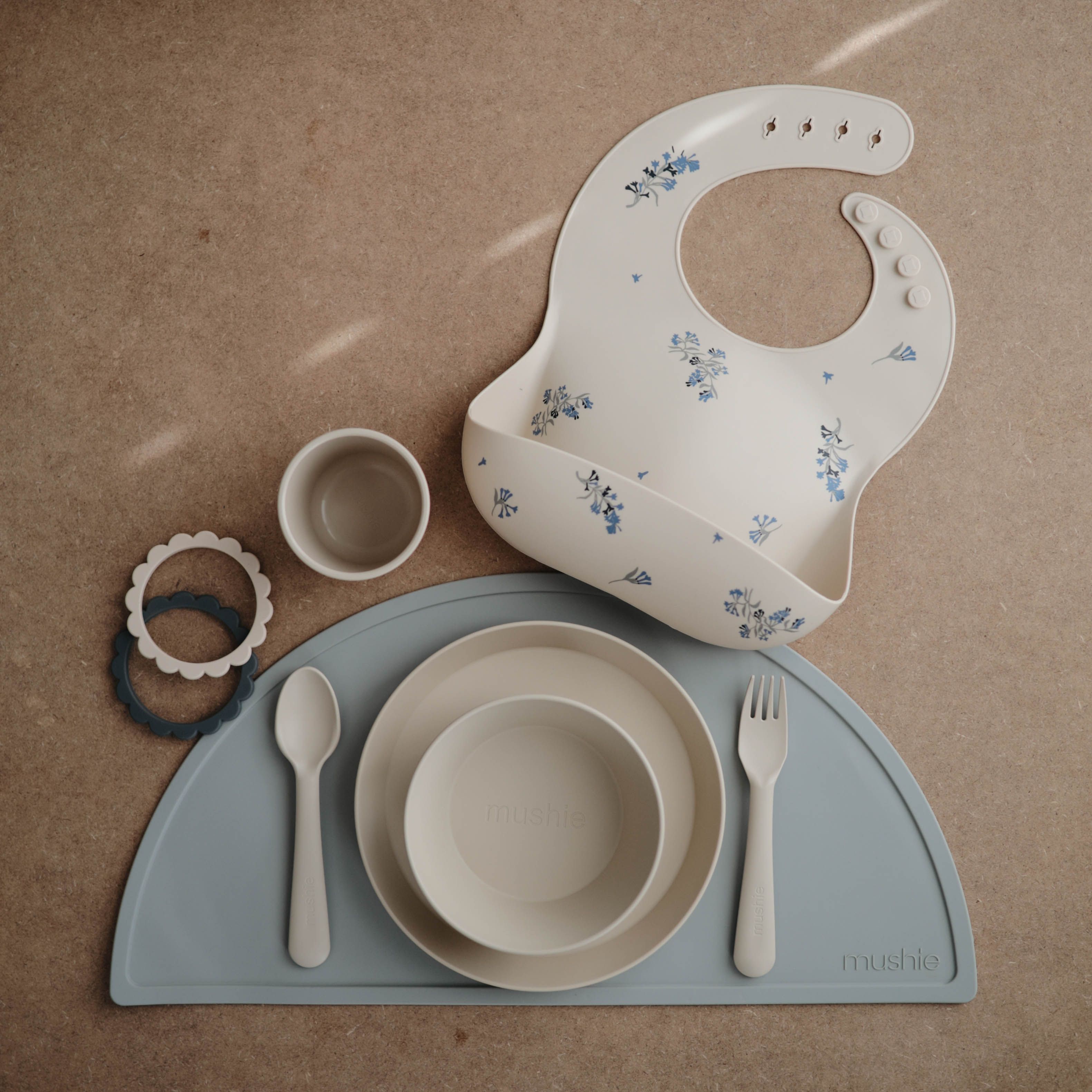Various Mushie dinnerware products - silicone bib, round bowl, round place, cutlery and placemat