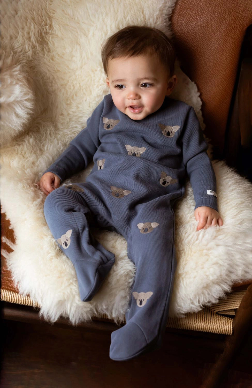 Donsje Phlyn Koalas onesie in Dark Spruce, worn by a baby on a chair
