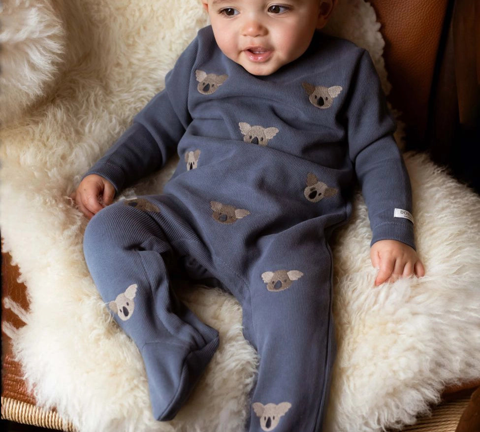 Donsje Phlyn Koalas onesie in Dark Spruce, worn by a baby on a chair