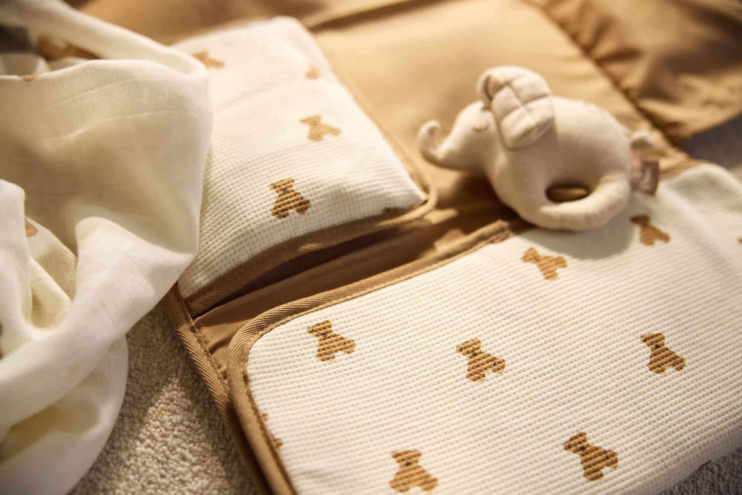 Jollein Little Waffle Mini Teddy Bear changing pad opened on a bed beside a teddy bear rattle