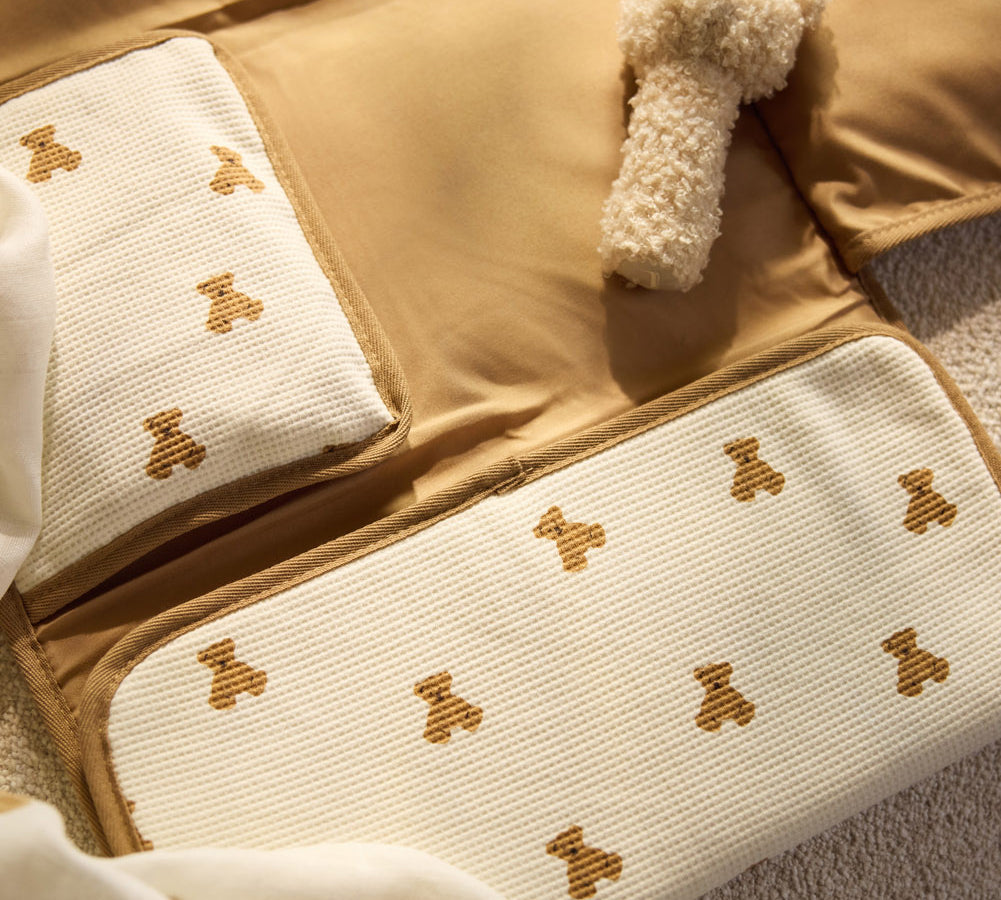 Jollein Little Waffle Mini Teddy Bear changing pad with the Natural Teddy Bear rattle on a bed