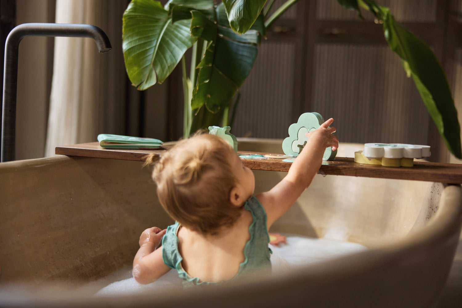 Child reaching toward Jollein Kangaroots bath puzzle pieces from inside a bathtub
