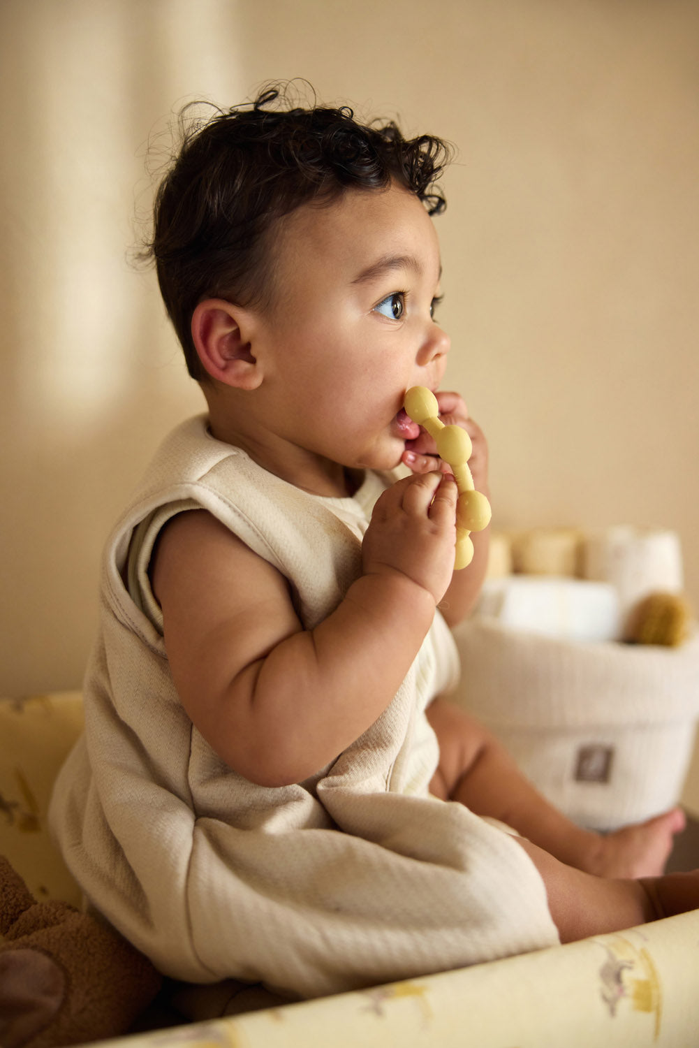 Baby seated while holding the Jollein Vanilla sun silicone teething ring near their mouth