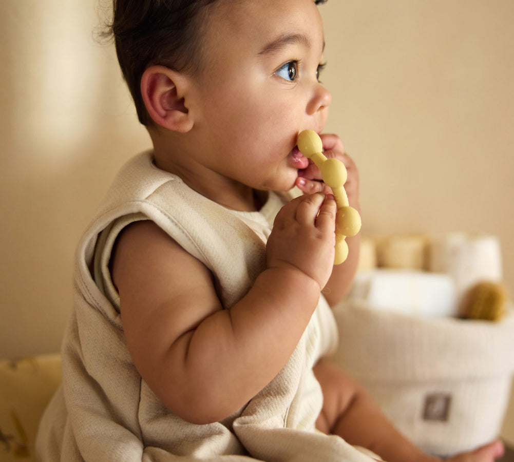 Baby seated while holding the Jollein Vanilla sun silicone teething ring near their mouth
