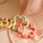 Jollein silicone flower toy loops in pink, green and yellow on pink fabric