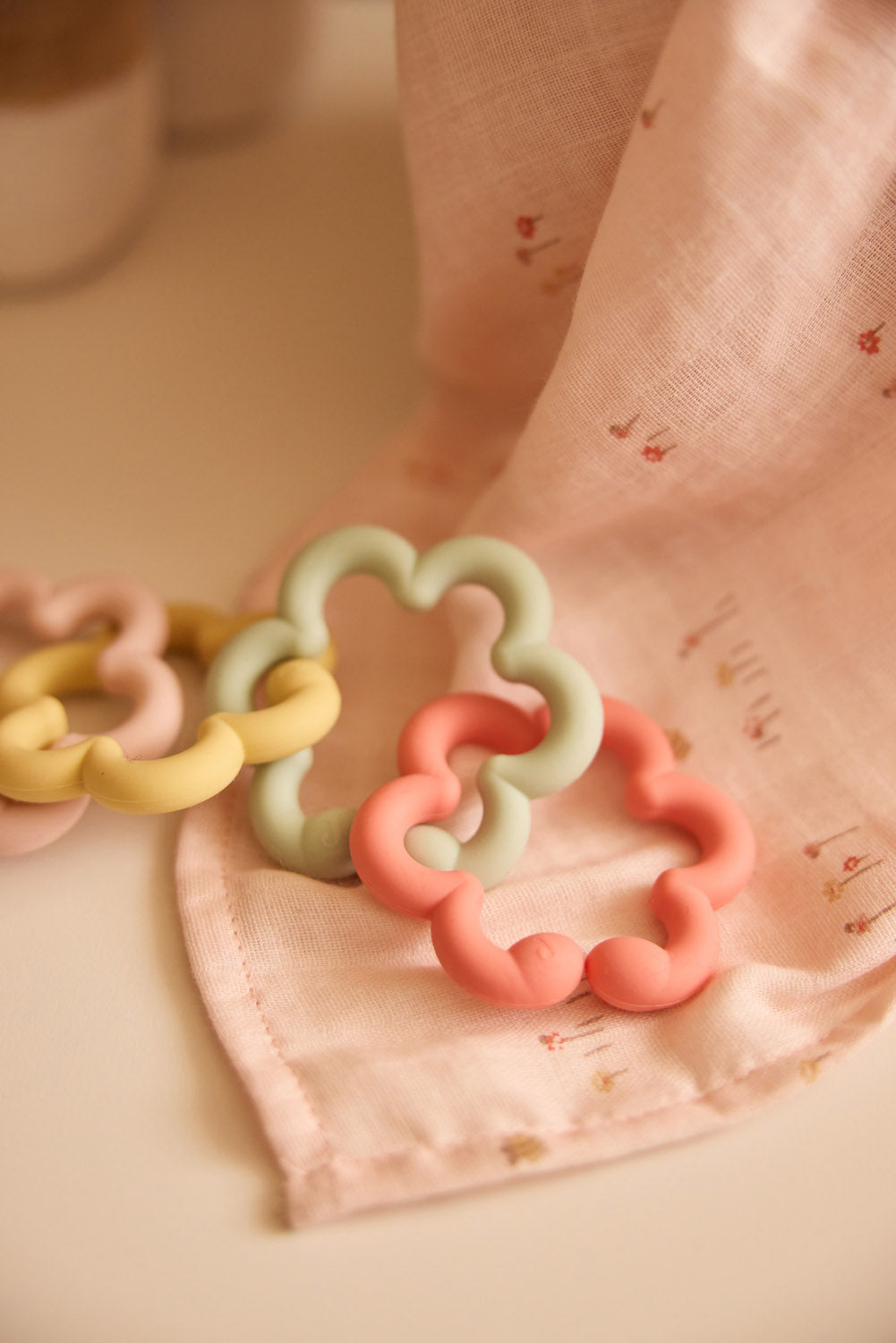 Jollein silicone flower toy loops in pink, green and yellow on pink fabric