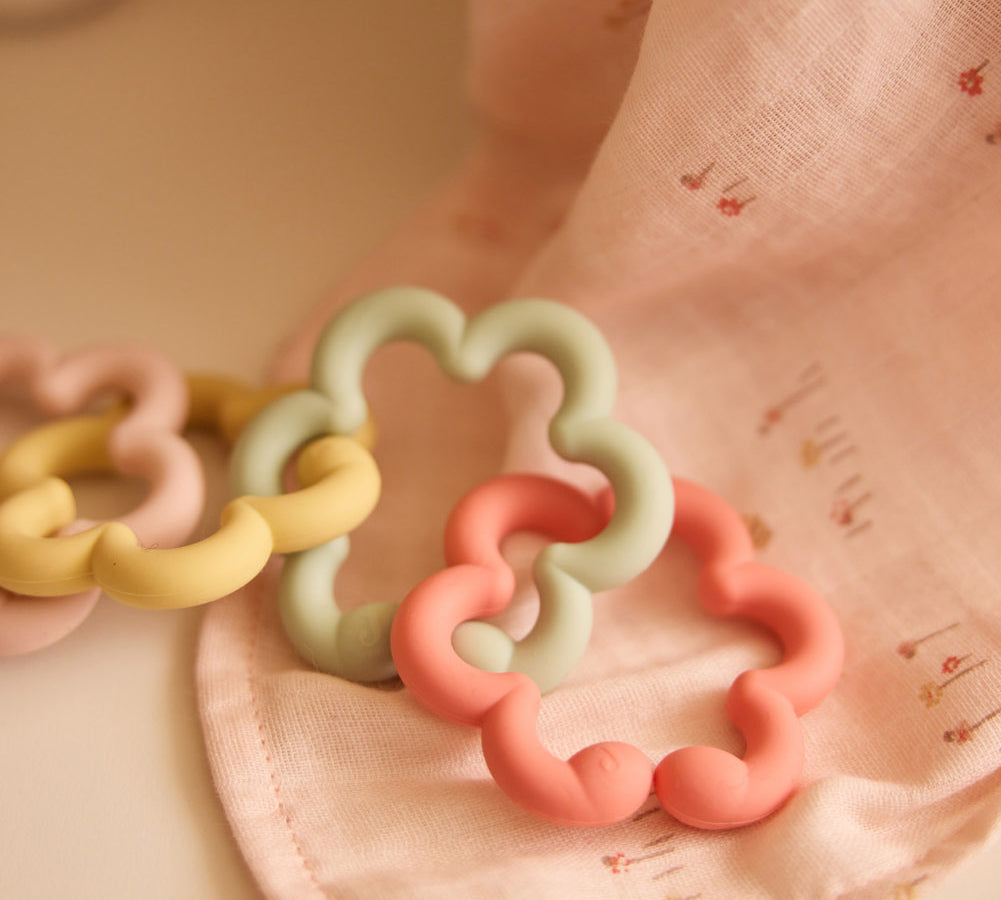 Jollein silicone flower toy loops in pink, green and yellow on pink fabric