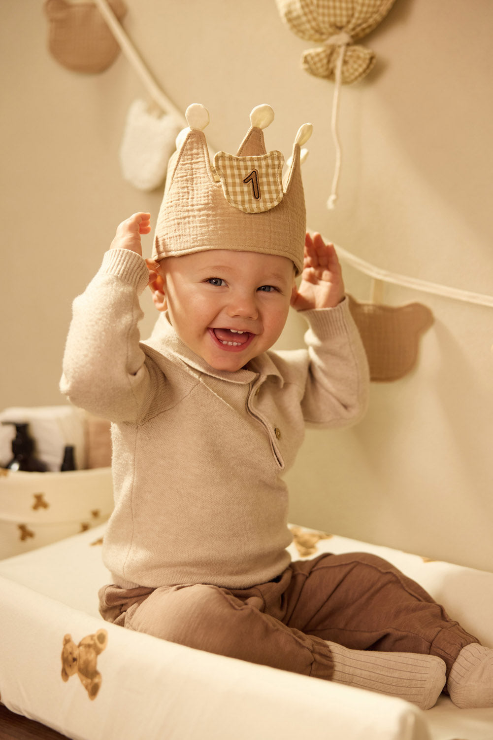Child wearing a Jollein Teddy Bear birthday crown with number 1 while seated on a Teddy Bear changing-pad cover