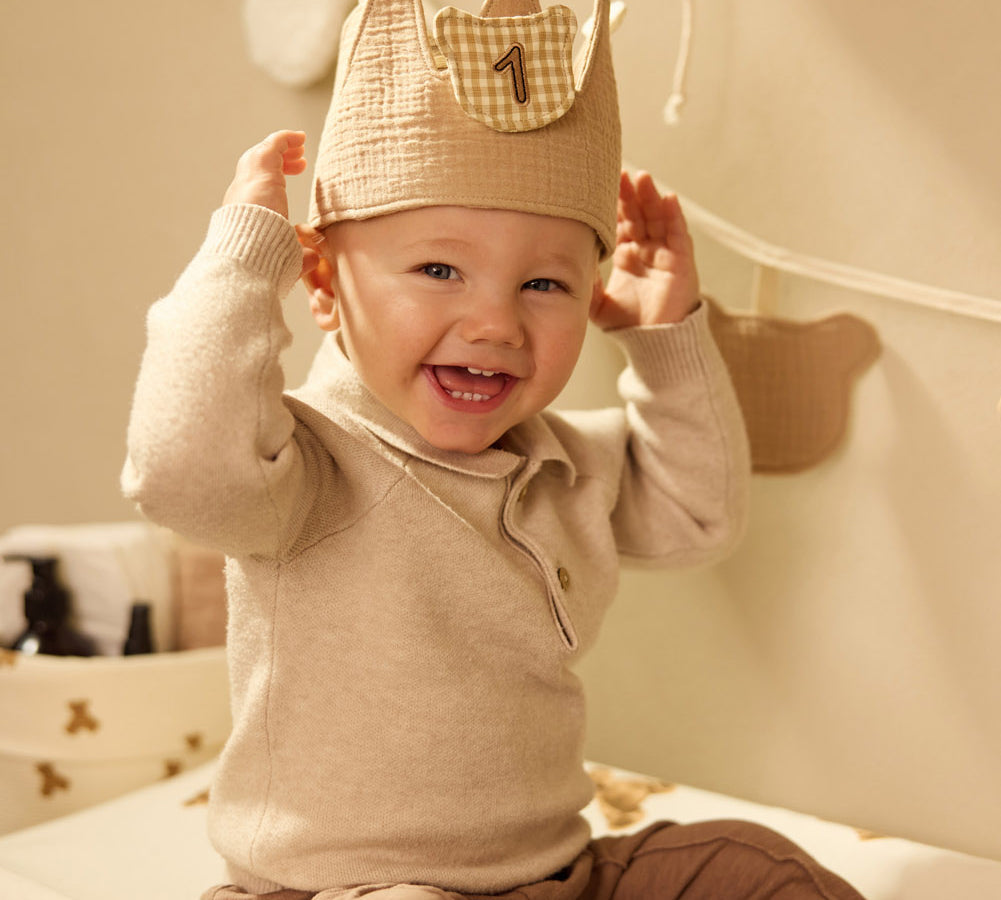 Child wearing a Jollein Teddy Bear birthday crown with number 1 while seated on a Teddy Bear changing-pad cover