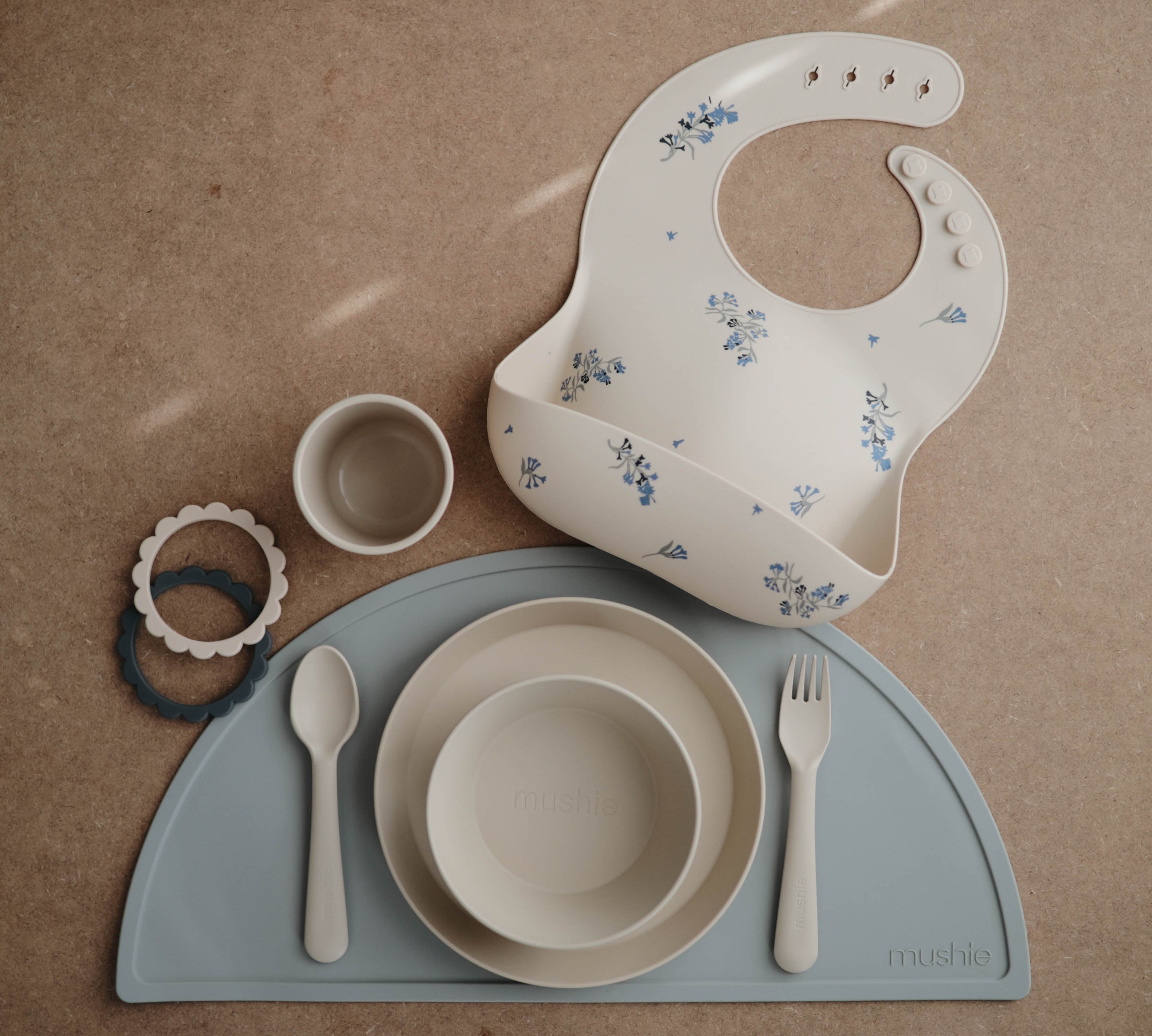 Various Mushie dinnerware products - silicone bib, round bowl, round place, cutlery and placemat