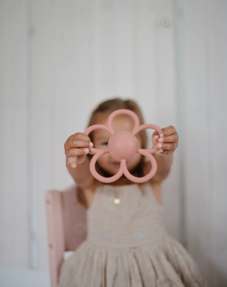 Girl holding the Mushie Rattle Teether Daisy 